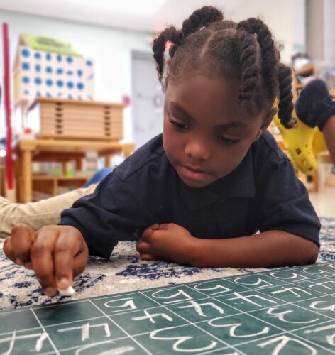 Kindergarten student laying down and writing numbers on a chalkboard
